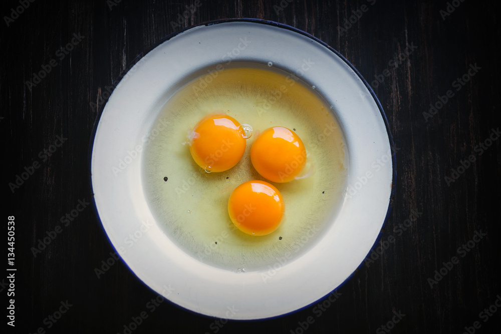 Three raw eggs in white metal plate on a black background Three raw eggs in white metal plate on a black background
