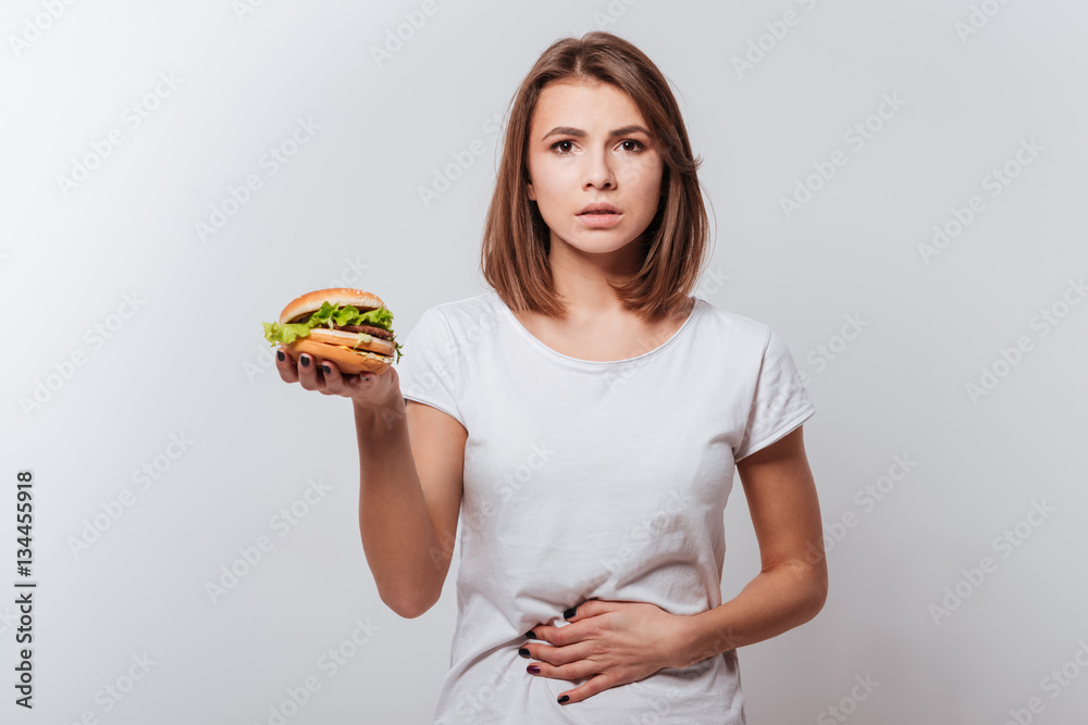 Confused young woman holding fastfood and touching belly Confused young woman holding fastfood and touching belly