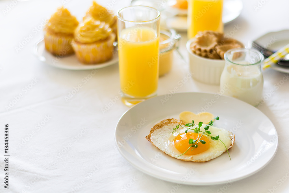Traditional breakfast with fried egg, yogurt, homemade muffins, citrus curd and orange juice on white background. Selective focus. High key Traditional breakfast with fried egg, yogurt, homemade muffins, citrus curd and orange juice on white background. Selective focus. High key