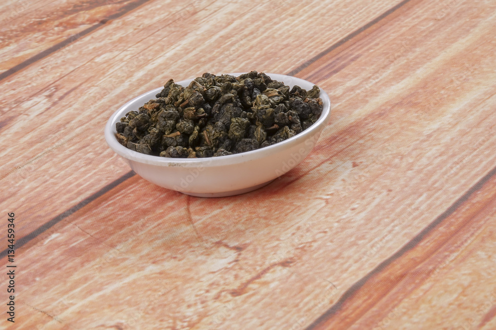 dried chinese tea leaves in a small bowl over wooden background dried chinese tea leaves in a small bowl over wooden background