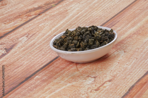 dried chinese tea leaves in a small bowl over wooden background