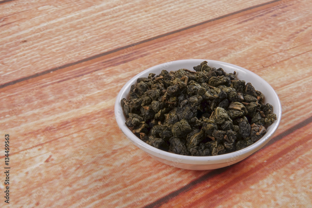 dried chinese tea leaves in a small bowl over wooden background dried chinese tea leaves in a small bowl over wooden background