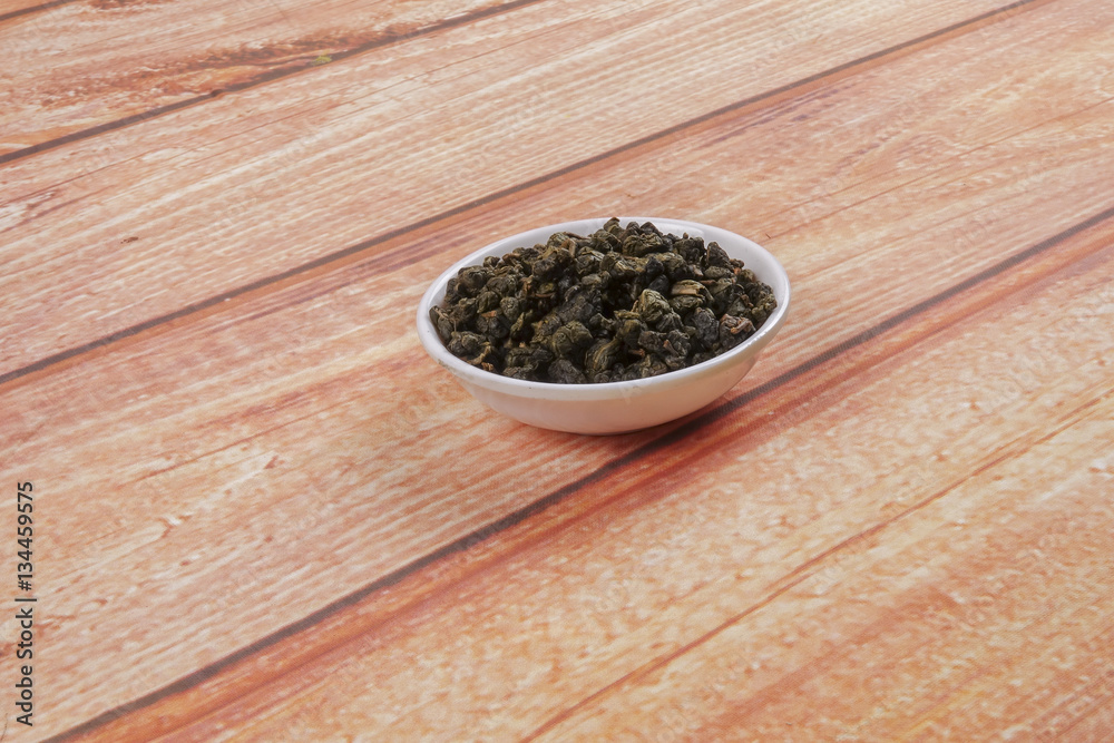 dried chinese tea leaves in a small bowl over wooden background dried chinese tea leaves in a small bowl over wooden background