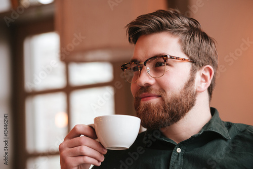 Smiling bearded young man drinking coffee.