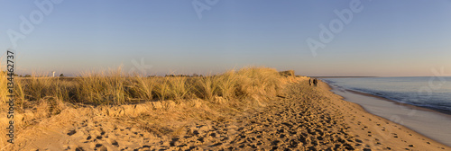 panoramic picture with people walking on the beach by romantic winter sunset