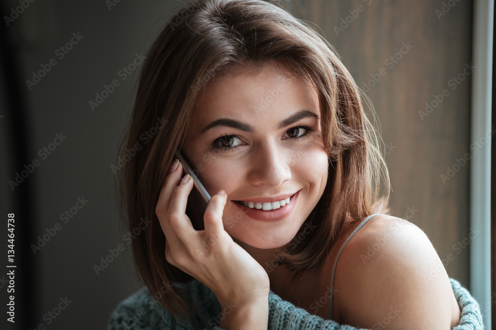 Smiling young lady sitting near window and talking by phone. Smiling young lady sitting near window and talking by phone.