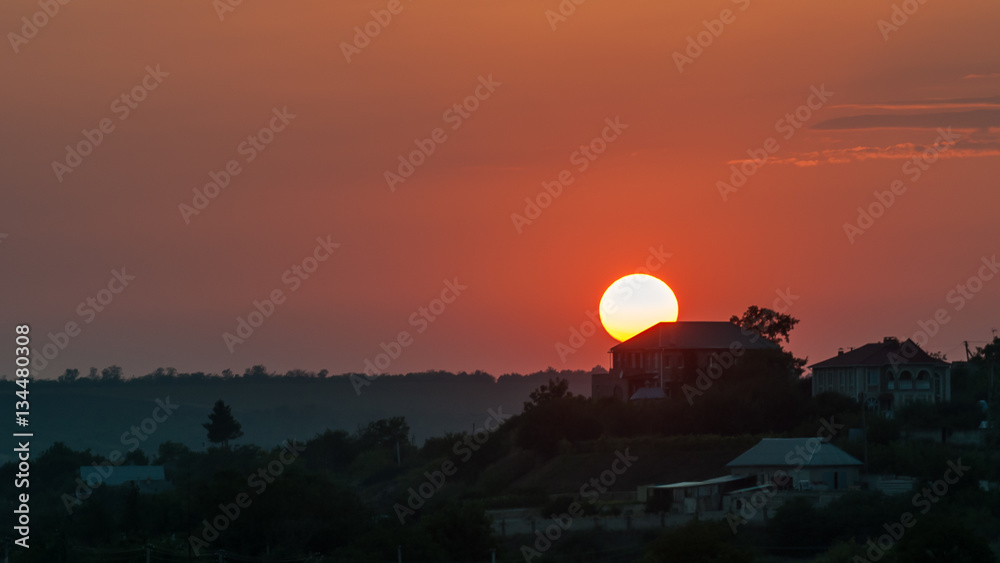 The sun sets on the background of the rural house. Red, orange sunset, landscape.