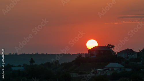 The sun sets on the background of the rural house. Red, orange sunset, landscape.