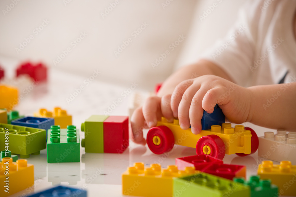 Close up of child's hands playing with colorful plastic bricks at the table. Toddler having fun and building out of bright constructor bricks. Early learning. stripe background. Developing toys Close up of child's hands playing with colorful plastic bricks at the table. Toddler having fun and building out of bright constructor bricks. Early learning. stripe background. Developing toys