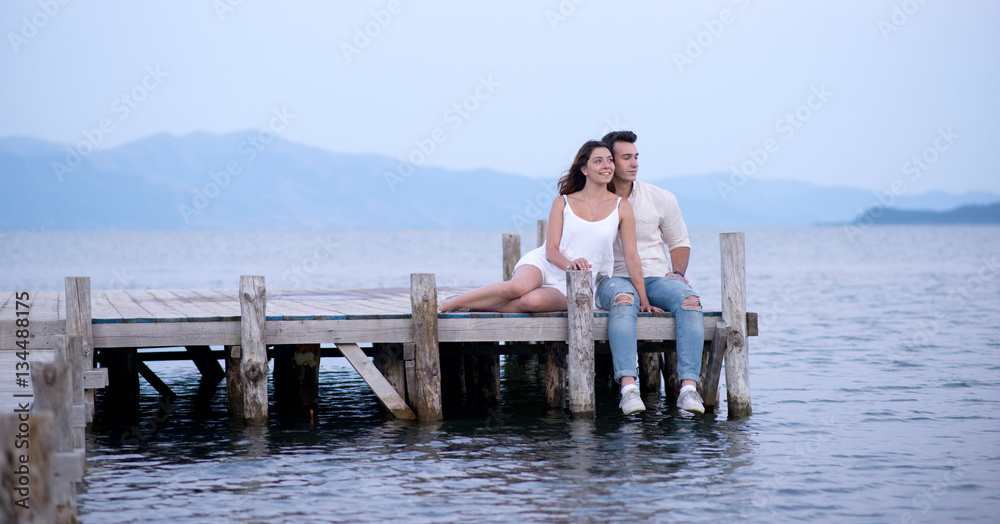 Happy couple sitting on a pier on summer vacation