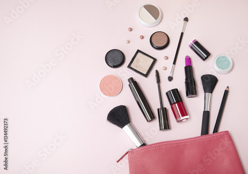 A pink leather make up pouch with cosmetic beauty products spilling out on to a pastel background, with empty space at side