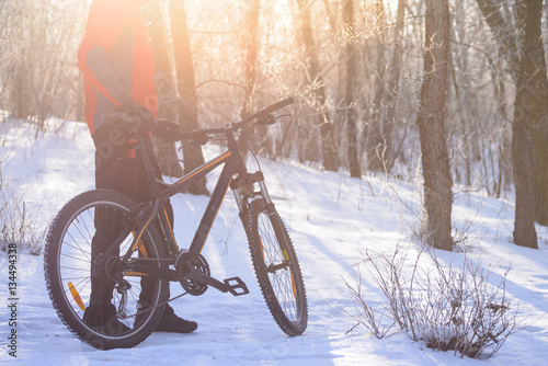 Mountain Biker with his Bike on the Snowy Trail in the Beautiful Winter Forest Lit by Sun © Maksym Protsenko