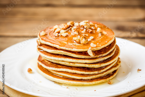 Pancakes with honey and walnuts on rustic wooden background
