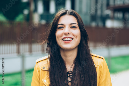 Portrait of young beautiful caucasian brown hair woman outdoor in the city looking at camera smiling - happiness, having fun, serene concept photo