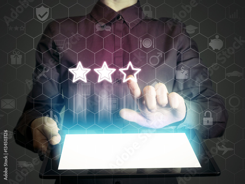 Concept of online rating. Person (man or woman) touches to the three stars (rating icon). Person  holds tablet pc, that contains a many different online services.
