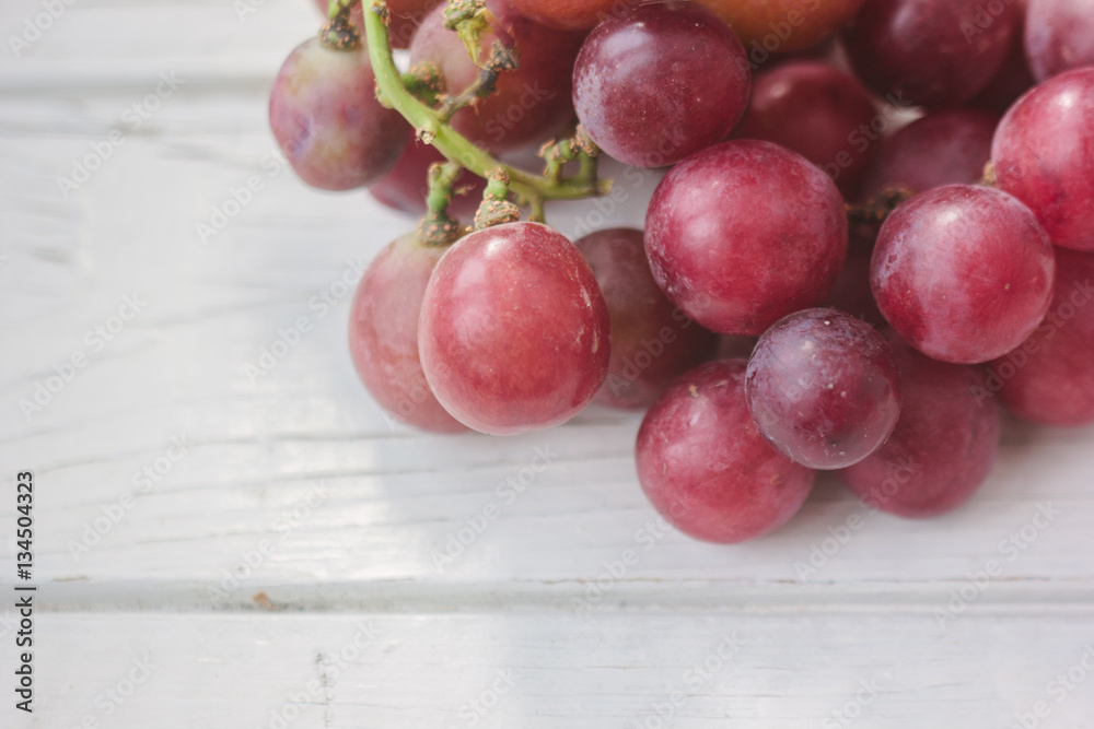 Red grapes over the white wooden board.