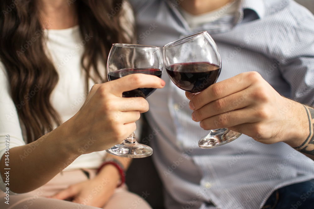 Close up of hands of young loving couple clinking glasses of red wine.