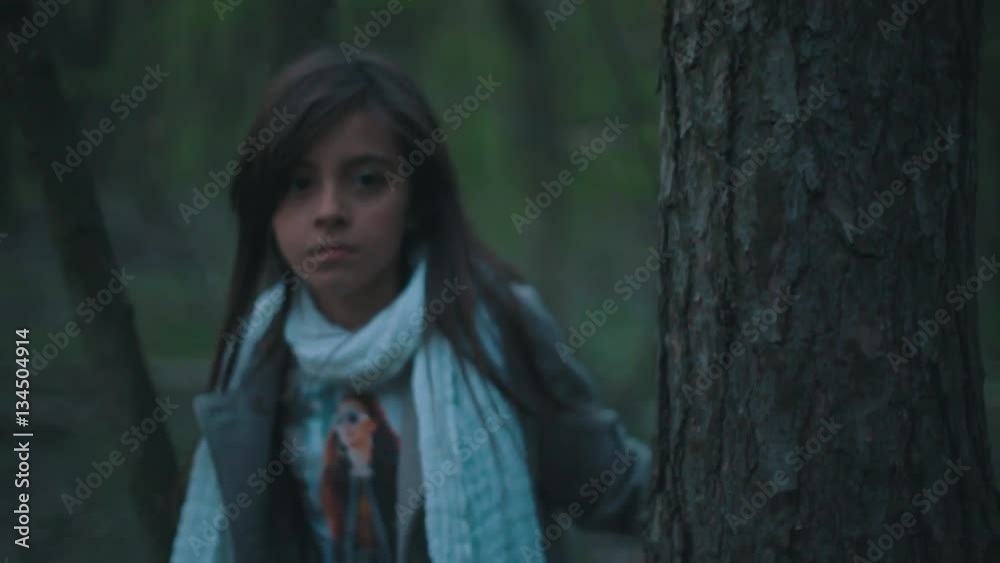 Little European brunette girl in a stylish look. Frightened lonely girl is wondering in the dark forest, she looks around and moving forward in the forest. Fearful atmosphere. Little European brunette girl in a stylish look. Frightened lonely girl is wondering in the dark forest, she looks around and moving forward in the forest. Fearful atmosphere.