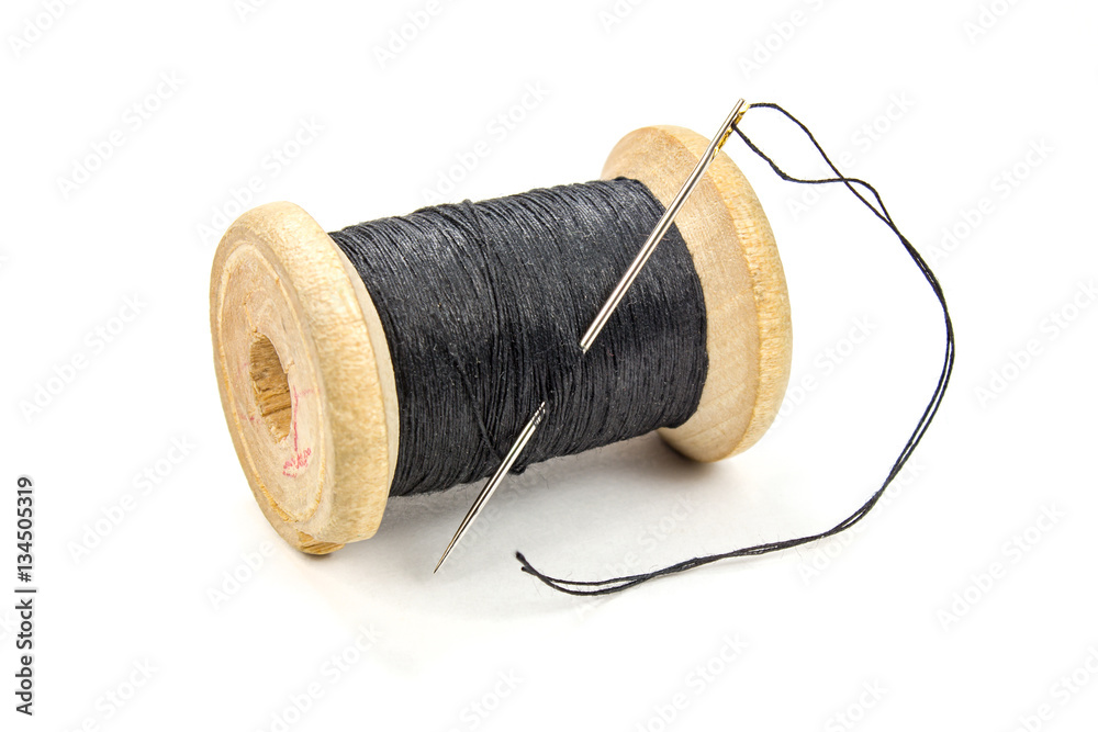 Vintage wooden spool of black thread and needle on white