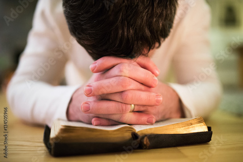 Unrecognizable man praying, kneeling on the floor, hands on Bibl