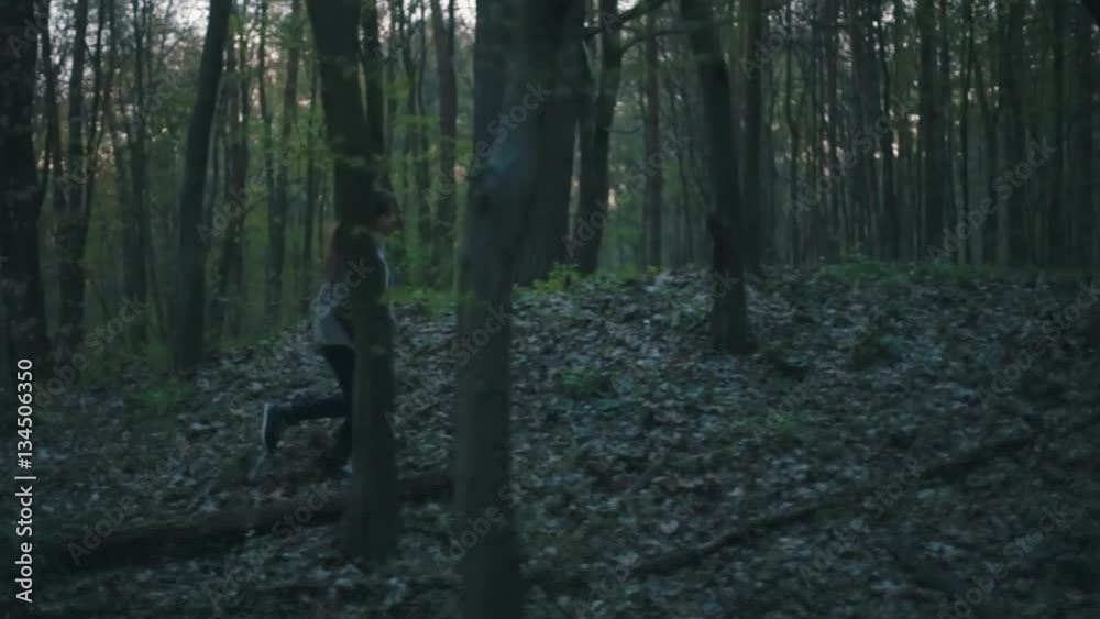 Little European girl with a long hair, brown jacket, black pants, sneakers and bright blue scarf. A scared little child is running through the dark deserted forest. Nightmare, loneliness.