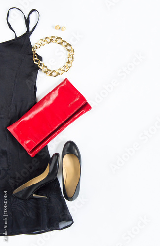 Cocktail dress outfit, night out look on white background. Little black dress, red clutch, black shoes, gold necklace and earrings. Flat lay, top view