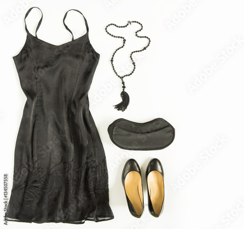Cocktail dress outfit, night out look on white background. Little black dress, evening bag, black shoes, black tassel necklace. Flat lay, top view