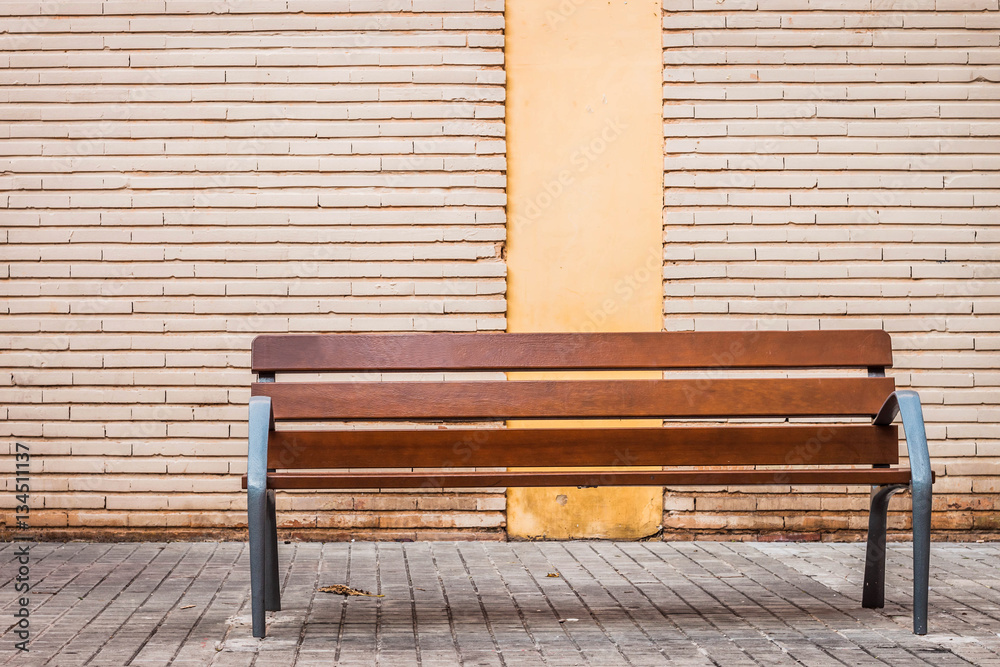 Wood bench on a city street with brick wall behind Stock Photo