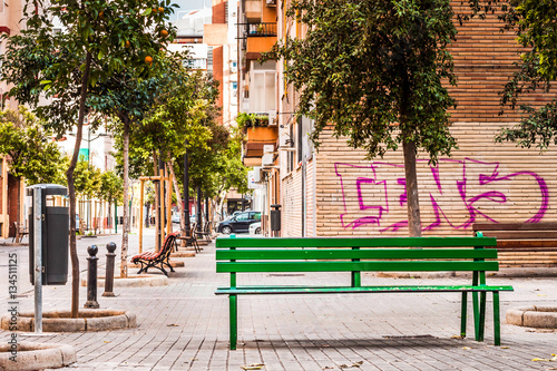 Fototapeta Naklejka Na Ścianę i Meble -  Bench on city street in summer with green trees around