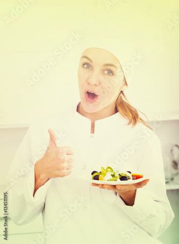 portrait of young coosie woman showing salad at kitchen photo