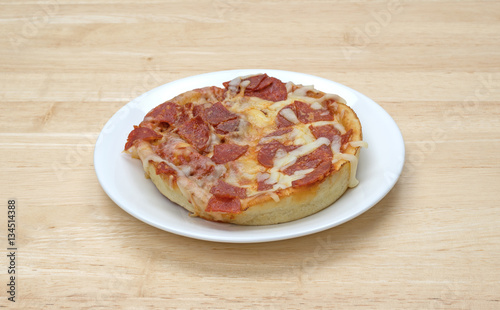 Personal size pepperoni pizza on a white plate atop a wood table.