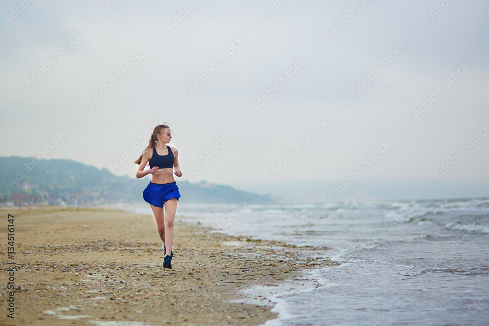 Young fitness running woman jogging on beach