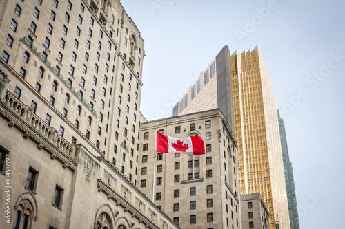 Photography Canadian flag in front of a business building and an older skyscraper in Toronto, Ontario, Canada