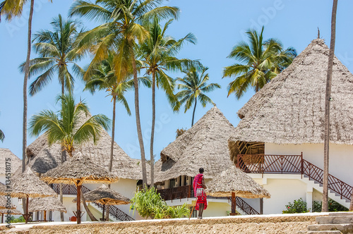 Beach huts and palm trees with man in traditional Masai Mara tribal dress at tropical African island beach destination