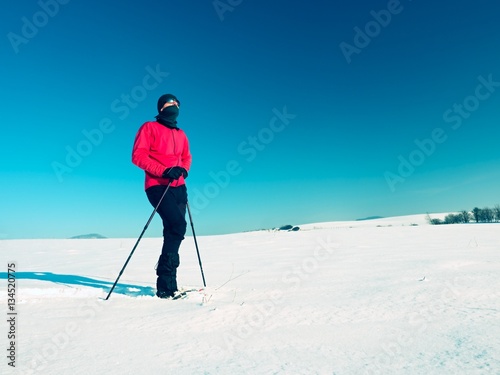 Winter tourist with snowshoes walk in snowy drift. Hiker in pink sports jacket