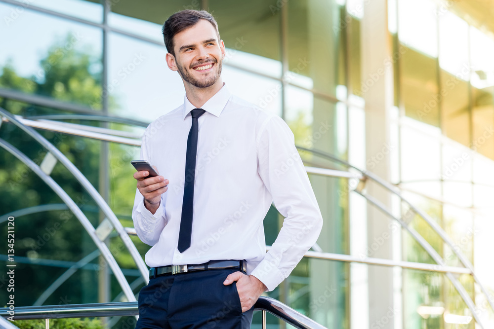 Fototapeta premium Confident young businessman in a suit standing outdoors smiling