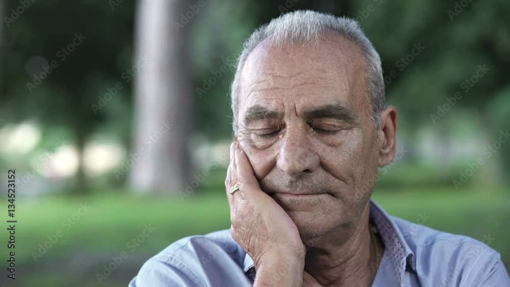  sad old man at the park holding hand on cheek