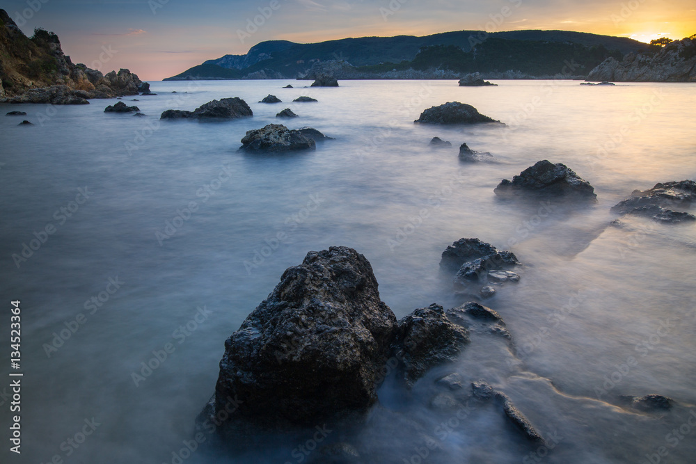 Fototapeta premium Long exposure seascape at sunrise. View of the cliff into the sea and distant islands. Paleokastrica. Corfu. Ionian archipelago. Greece.