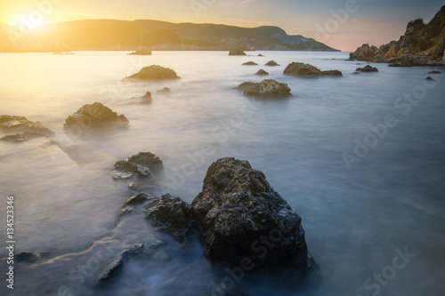 Long exposure seascape at sunrise. View of the cliff into the sea and distant islands. In the backlight sunbeam light. Paleokastrica. Corfu. Ionian archipelago. Greece.