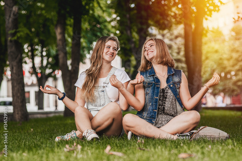 portrait of two beautiful young women best girlfriends having fun relaxing in the park sitting on the grass happy smiling