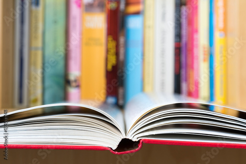 An open book in foreground with a blurred colorful library in background