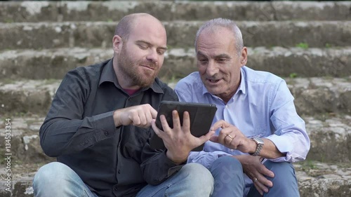 Father and son sitting outdoors watching the tablet photo