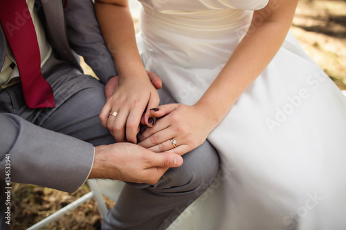 Bride and groom holding hands with engagement rings on fingers at wedding day