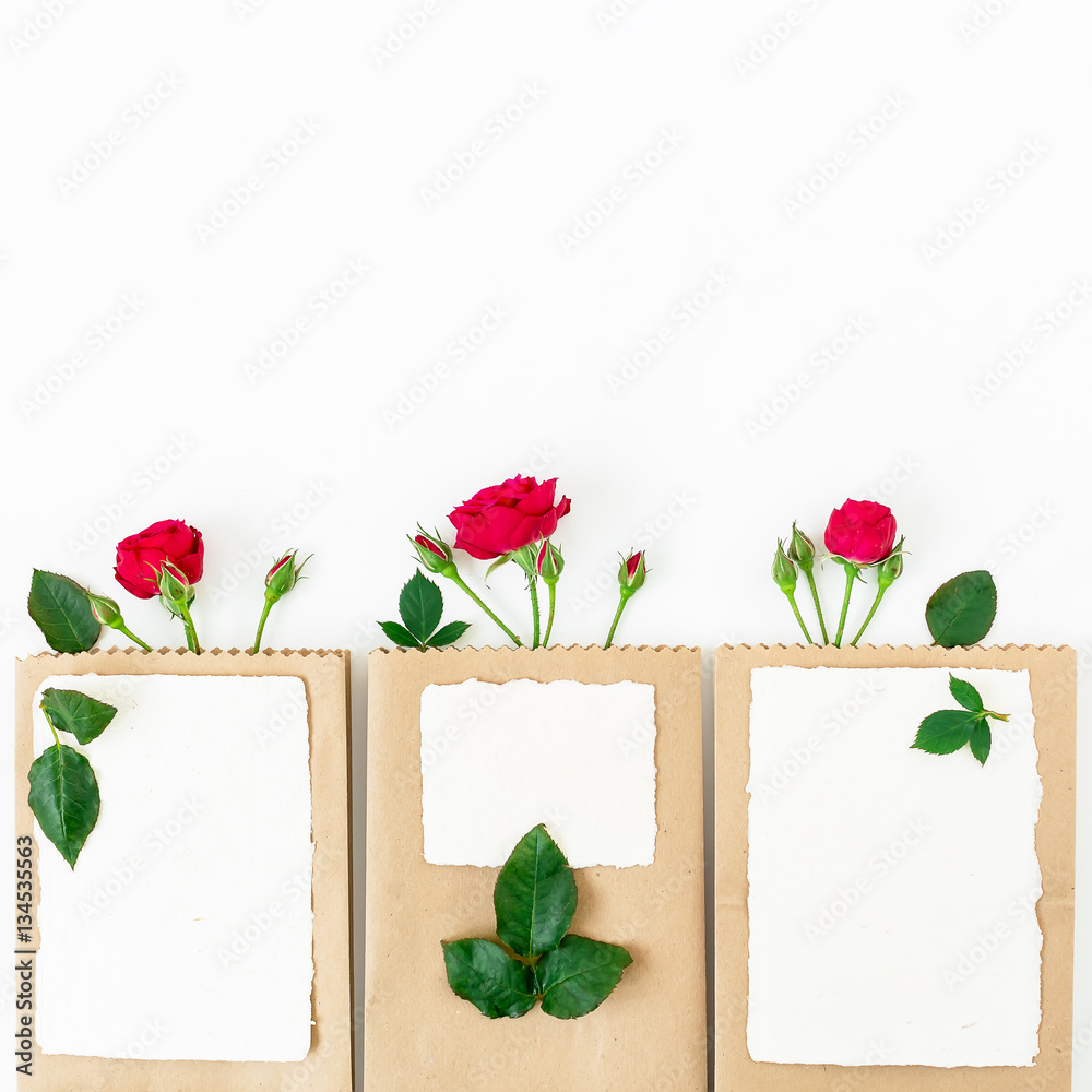 Red roses, branches, leaves, paper cards and craft pack isolated on white background. Flat lay, top view