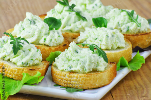 Cream cheese bites with arugula and herbs, savory party canapes on white plate.