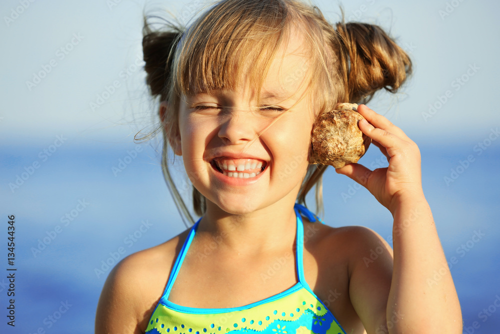 Fototapeta premium Cute girl listening to seashell at sea