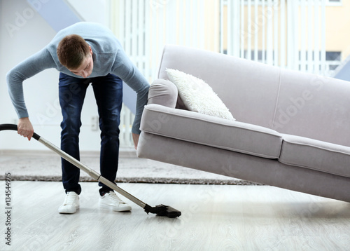 Young man with vacuum cleaner cleaning floor at home photo
