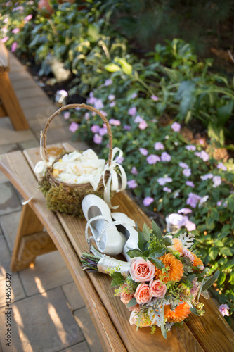 Flower Basket, Flower Girl's Shoes, and Bridesmaid's Bouquet on Wooden Bench