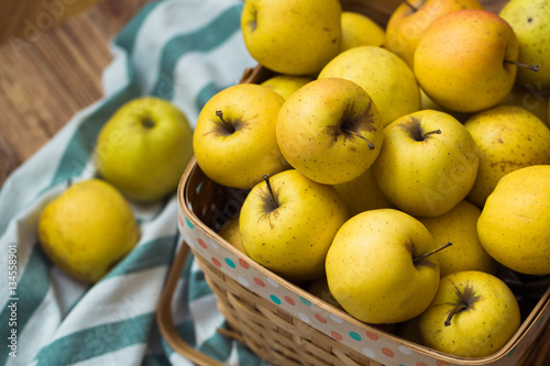 Golden apples in a basket on a wooden background
