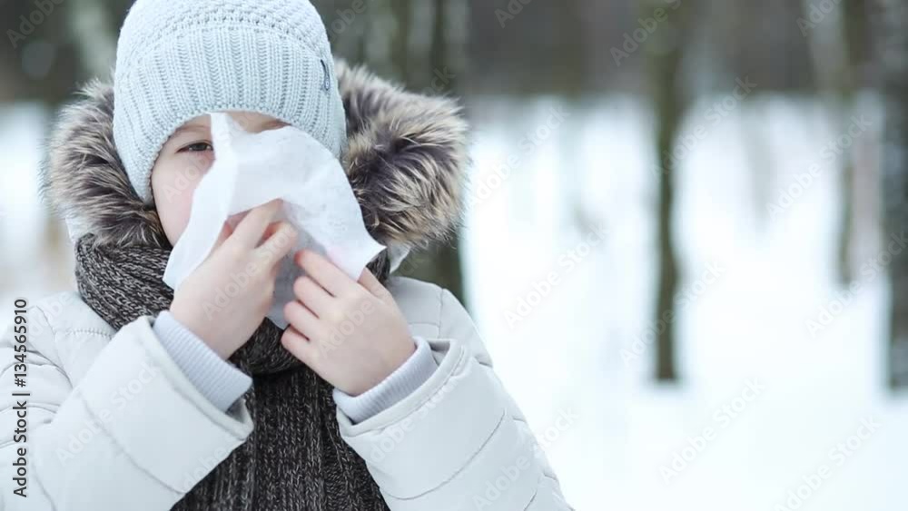 Girl wipes her nose with a tissue in the winter park